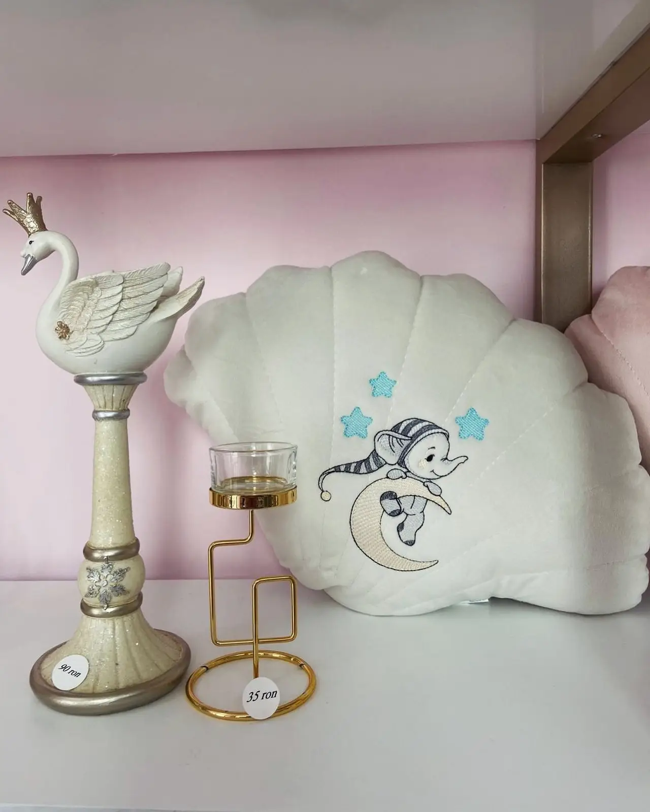 Pernă albă în formă de scoică brodată cu lună și iepuraș, lângă o lebădă decorativă