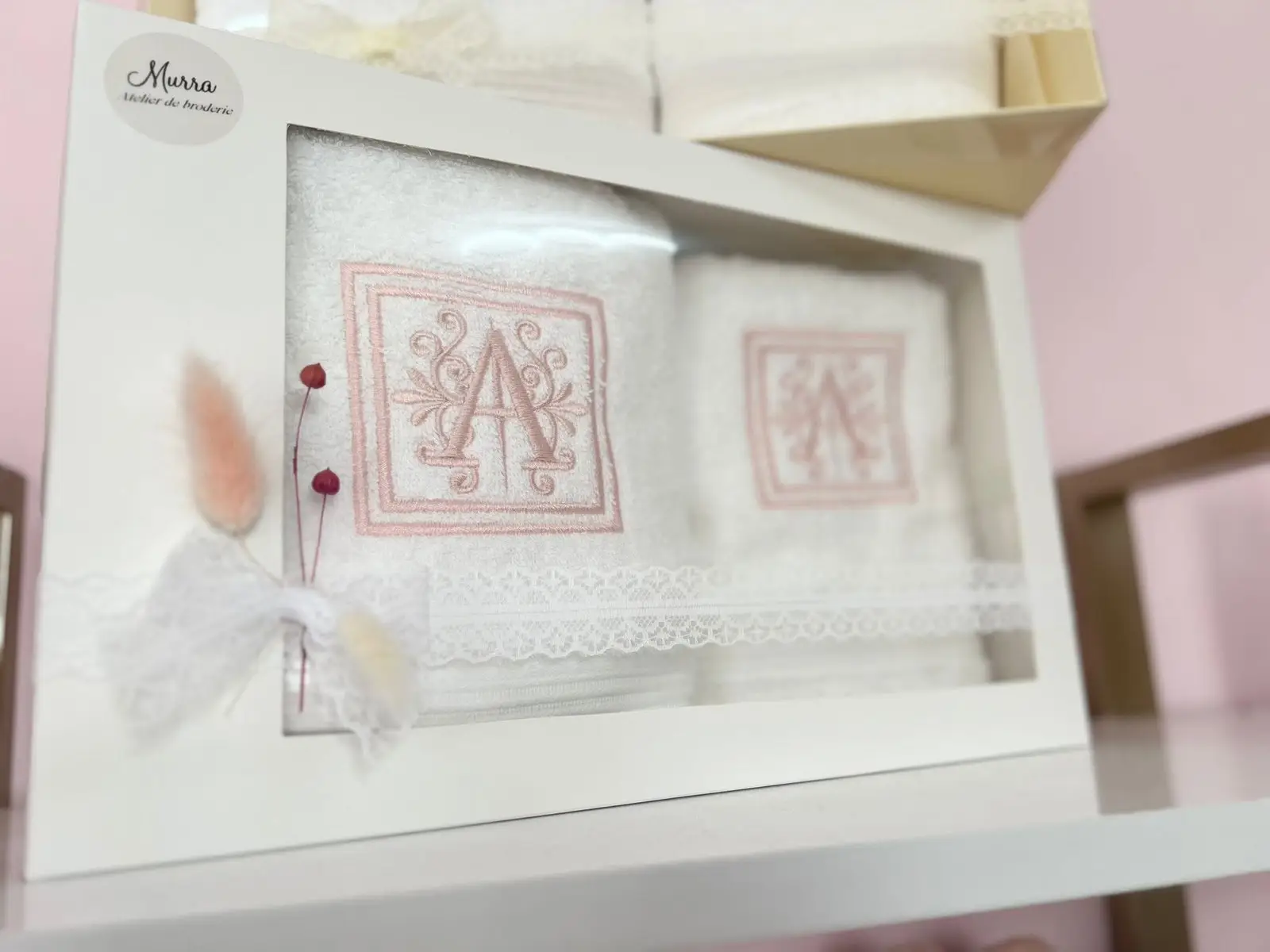 Cutie cadou albă cu prosoape brodate cu inițiala A în roz și decor cu pene